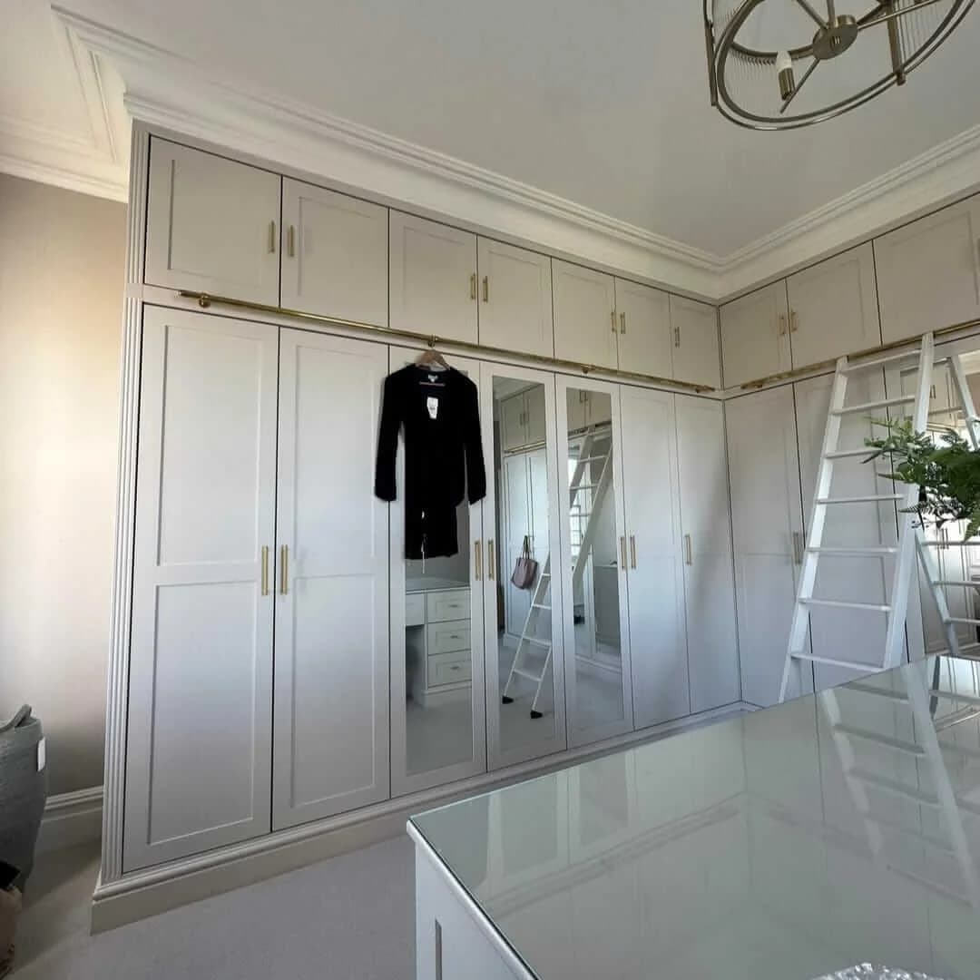 A bespoke walk-in dressing room with mirrored wardrobe doors and a brass hanging rail