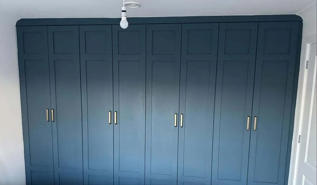 A navy blue floor-to-ceiling fitted wardrobe with brushed-brass handles